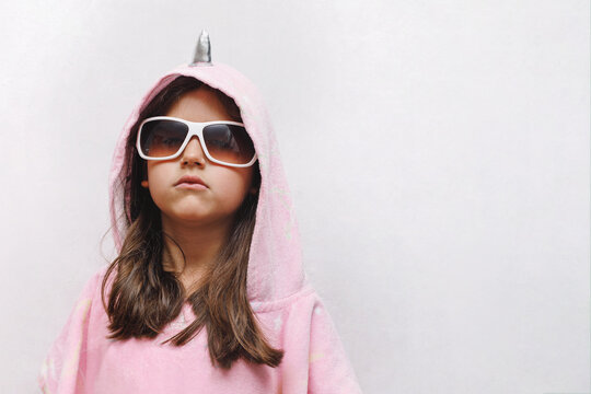a little girl in a pink poncho and sunglasses is very serious, a funny child in a unicorn costume on a white background