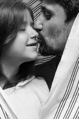 A brunette father with a beard hugs and kisses his daughter, close-up, white background