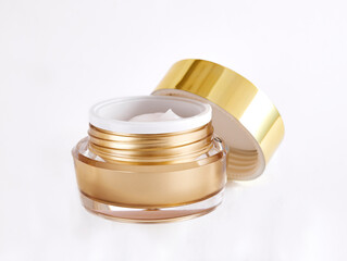 Cosmetic jar with open golden cap containing moisturizing cream for face isolated on white background