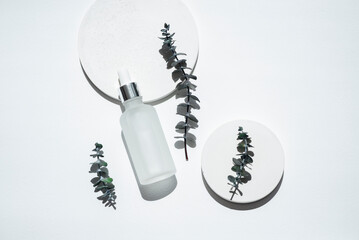 Transparent frosted glass dropper bottle with eucalyptus branches. White background with daylight....