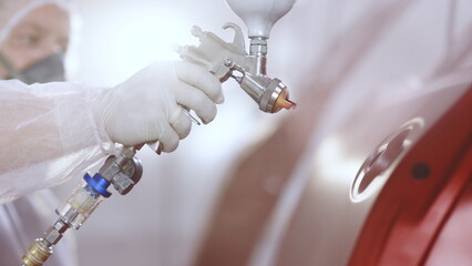 Auto painter spraying red paint on the rear door of the car in special booth. Painting vehicle parts at car service workshop. Modern car painting