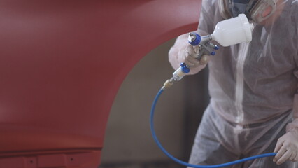 Red car in a paint chamber during repair work. Auto painting worker. Professional car painter is...