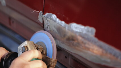 Close-up of worker grinds car damage. Hard grinding is designed to smooth out irregularities....