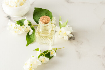 glass vial with organic jasmine oil, mortar and pistil with flowers on a marble white background....