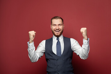 Handsome businessman smiling against red studio wall background. Business win, fun and success concept