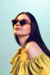 Portrait of young girl in stylish dress and trendy sunglasses posing isolated over green studio...