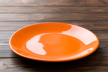 Perspective view of empty orange plate on wooden background. Empty space for your design