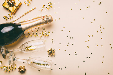 Bottle of champagne with colored glitter, confetti and gift box space for text on colorfull background, top view. Hilarious, christmas and birthday celebration