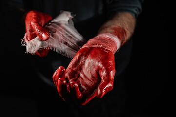 A man covered in blood bandages his hands.