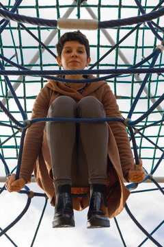 Low Angle Shot Of A Pretty Adult Woman Inside A Rope Exterior Game For Kids Looking Down At Camera With The Sky In The Background