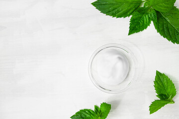 A smear of cosmetic white cream on a white wooden table with green mint leaves. Organic cosmetics...