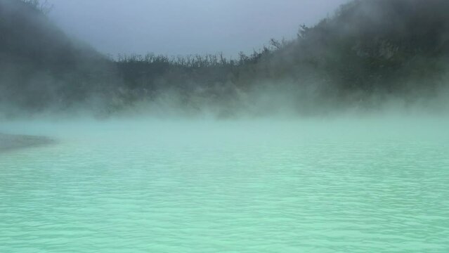 spooky landscape with steam rising from green sulfur lake in Kawah Putih volcano crater in Bandung Indonesia