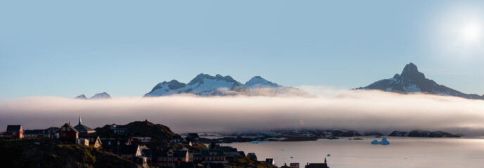 A layer of fog spreads between the mountains and the sea -Picturesque village and Colorful houses on coast of Greenland - Tasiilaq, East Greenland