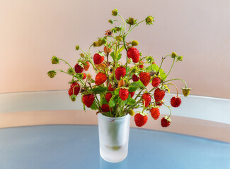 Cute bouquet of ripe wild strawberries stands on a glass table. Close-up.