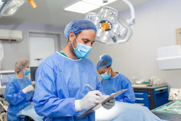 Surgeon writing on clipboard in operation room, anaesthesiologist writing the updates