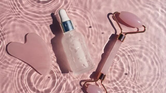 Cosmetic bottle with pipette and Massage roller on water with drops on a pink background. Pure water with reflections sunlight and shadows. Video of packaging for advertising, products High quality 4K