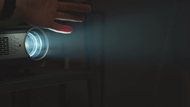 Slowmo closeup of unrecognizable hand touching light from turned on slide projector in dark room