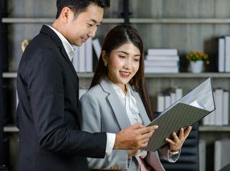 Asian young professional businesswoman secretary sitting smiling working showing graph chart paperwork document report to successful businessman entrepreneur in formal suit drinking coffee from cup