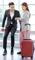 Asian young professional successful businessman and businesswoman colleague in formal suit standing together with trolley baggage in airport hallway waiting checking for business trip boarding time