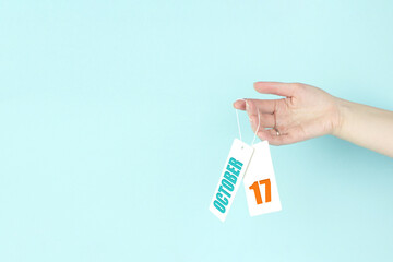 October 17th. Day 17 of month, Calendar date. Hand hold price tag with calendar date on blue background. Autumn month, day of the year concept.