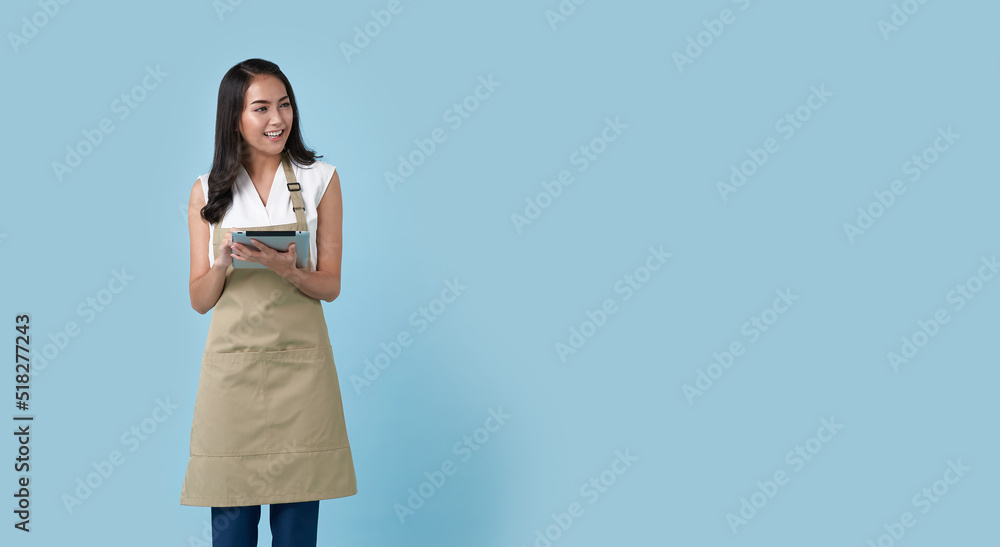 Wall mural young asian entrepreneur woman in apron hand holding tablet for list order food isolated on blue bac