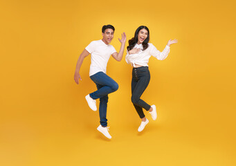 Fototapeta na wymiar happy excited young asian loving couple jumping isolated over yellow wall background.