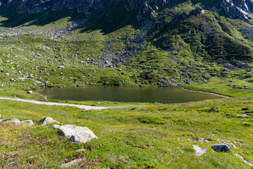 Fototapeta na wymiar Scenic landscape at hiking trail at Swiss mountain pass St. Gotthard with mountain lake and historic Tremola road on a sunny summer day. Photo taken June 25th, 2022, Gotthard Pass, Switzerland.