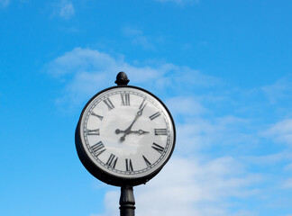 Fototapeta na wymiar Round clock with Roman numerals against the blue sky. Copy space. Time concept