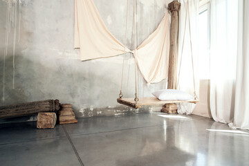 Fototapeta na wymiar Photo of modern concrete designer interior with wooden swing with pillow. Natural sunlight.