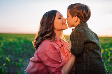 Fototapeta premium Tender scene of loving son with mom on sunset backdrop. Beautiful family. Cute 3 year old kid with mother. Parenthood, childhood, happiness, children wellbeing concept.