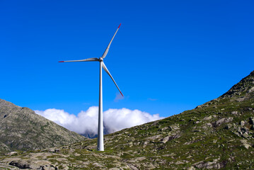 Wind turbine at Swiss mountain pass St. Gotthard with rocks and grass on a sunny summer day. Photo...