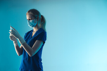 young lady nurse with a protective mask holiding a vaccination syringe - light blue background closeup. High quality photo