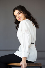 Beautiful smiling young woman wear in a white shirt, looking at camera posing in a studio, isolated grey wall background.