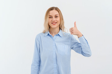 Happy good-looking young blonde woman in in blue casual style shirt, laughing and doing positive gesture with hand, thumb up. Indoor studio shot on white background