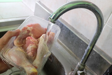 Thawing frozen chicken or poultry meat on running water on a sink. - obrazy, fototapety, plakaty