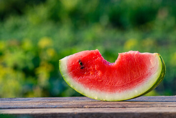 Delicious refreshing watermelon on the outdoors wooden  table, GREEN  natural background  Slice sunny day, Heap,  Fresh ripe red, leaf, summer sunny garden juicy organic  sweet fruit, vegan food