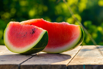 Delicious refreshing watermelon on the outdoors wooden  table, GREEN  natural background  Slice sunny day, Heap,  Fresh ripe red, leaf, summer sunny garden juicy organic  sweet fruit, vegan food