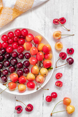 White plate with colorful cherries on a white background, Yellow and red cherries. Sweetfruit salad. Healthy eating concept. Top view.