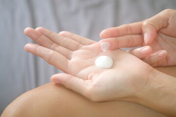 Asia woman sitting on bed and applying cream on her hand.