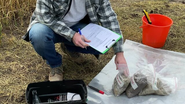 Agriculturist taking notes to soil sampling information sheet, checking sample bags, writing report at field. Specialist taking sample fertility analysis outdoors. Environment research, certification