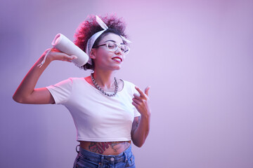 Young positive kazakh girl with afro hairstyle listens music in portable speaker, dances and poses,...