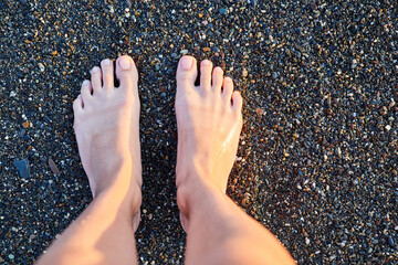 Women's feet stand on a wet pebble beach. Top view