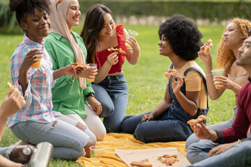 group of multiracial friends picnicking eating pizza and drinking drink, having fun in city park at...