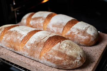 Homemade wheat loaves are baked in the oven on a baking stone. Close-up, selective focus