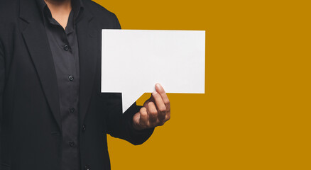 Close-up of hand businessman in a suit holding a blank white speech bubble while standing on an orange background