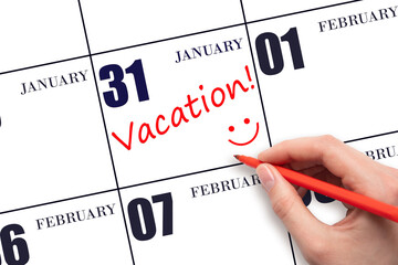 A hand writing a VACATION text and drawing a smiling face on a calendar date 31 January. Vacation planning concept.