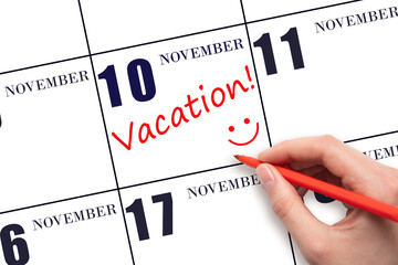 A hand writing a VACATION text and drawing a smiling face on a calendar date 10 November. Vacation planning concept.