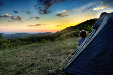 ein Kind beobachtet den Sonnenuntergang im Zelt sitzend
