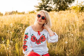 portrait of happy joyfull mature woman wearing traditional Ukrainian embroidered shirt - vyshyvanka in countryside during beautiful sunset