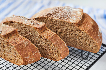 Sliced homemade round rye bread on a metal wire rack with a cloth. Close-up, selective focus